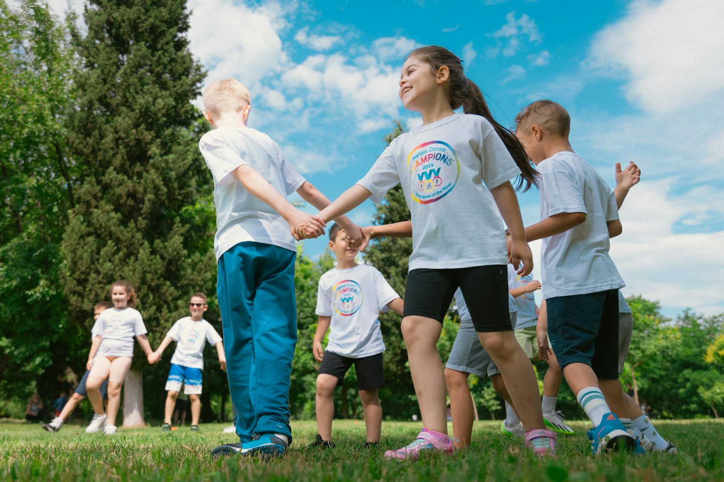 Children in matching shirts hold hands while playing outdoors.