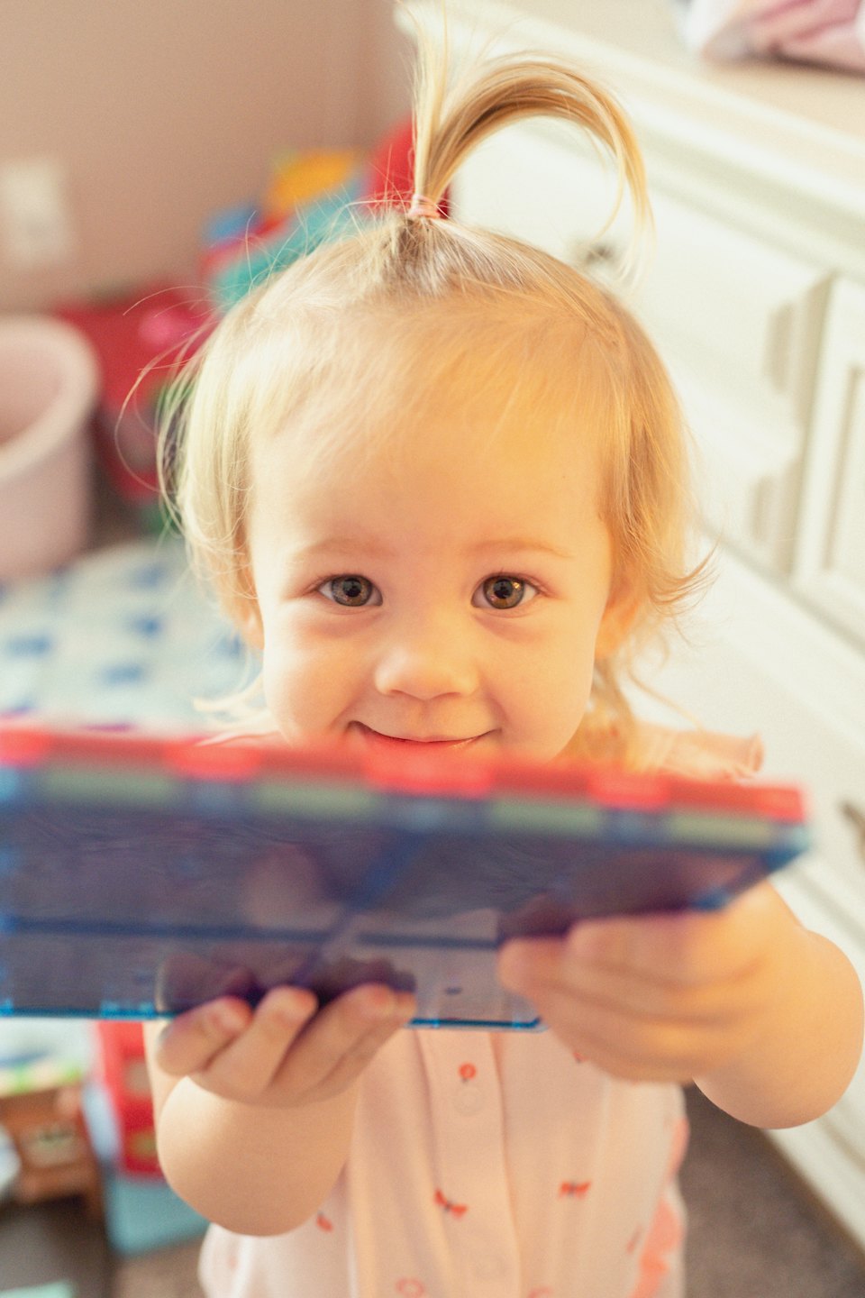 Toddler in a pink shirt holds blue and red magnetic tiles.