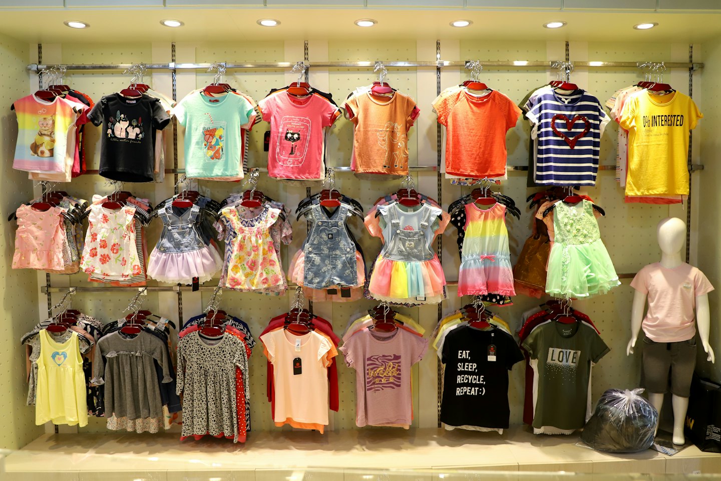Children's clothing hangs on racks beside a store mannequin.