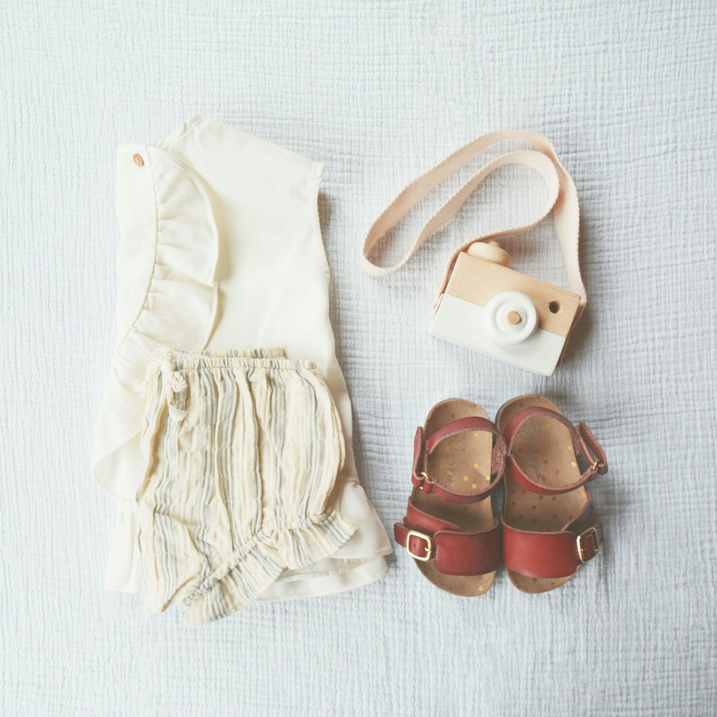 Children's outfit with wooden toy and red sandals on fabric.